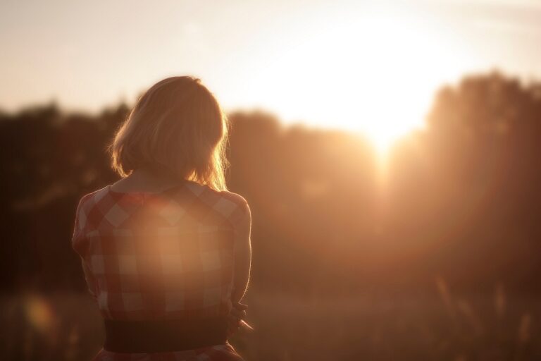 A woman stands alone watching a sunset, reflecting solemnly on her grief after losing her mother